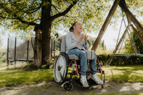 Eine Frau im Rollstuhl sitz im Garten und lässt sich die Sonne auf den Pelz scheinen